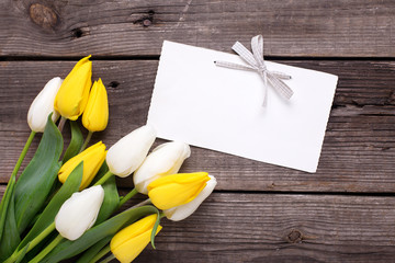 Empty tag and yellow and white tulips flowers  on  vintage wooden background.