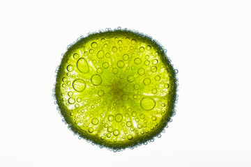 Fototapeta na wymiar Close-up of air bubbles covering slice of juicy lime floating in water