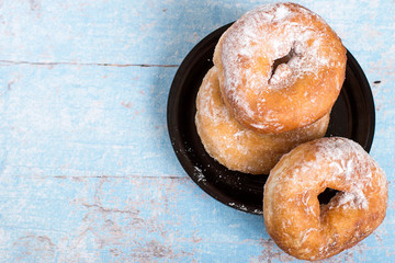  Homemade donuts.   Homemade donuts sprinkled with powdered sugar on  small black plate on a light wooden table. 