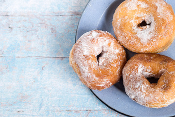 

 Homemade donuts.   Homemade donuts sprinkled with powdered sugar on a metal dish on a light wooden table.
