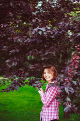 Obraz na płótnie Canvas Joyful young girl with red hair stnds under dakr green leaves