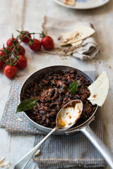 chili vegetariano di fagioli neri in primo piano, pane piatto e pomodori freschi su base rustica di legno