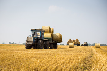 Fototapeta na wymiar Vinnitsa,Ukraine - July 26,2016.huge tractor collecting haystack in the field at nice blue sunny day,Tractor collecting straw bales,Agricultural machine collecting bales of hay,harvest concept