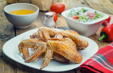 .Roasted chicken wings, salad, salt, vegetable oil, red pepper, tomatoes, chives on a rustic wooden table. Focus concept.