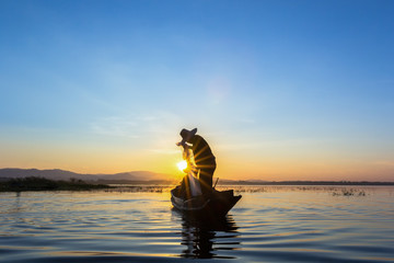 Silhouette fisherman on fishing boat setting net with sunrise 