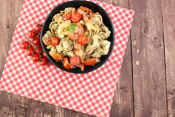 Bowl of tricolor tortellini pasta salad with tomatoes and onions on dark wood table background