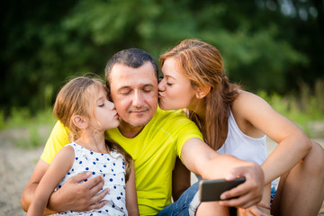 Father being kissed by daughters while taking a selfie