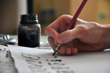 Creating of manual calligraphy. Hand with pen and ink close up.