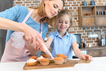 portrait of mother putting cream on cupcakes with daughter near by