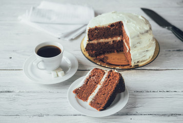 Piece of homemade cake and coffee on a white wooden table. Biscuit cake and knife at the background