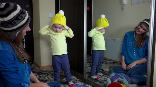 Playful family girls measuring warm winter hats near mirror