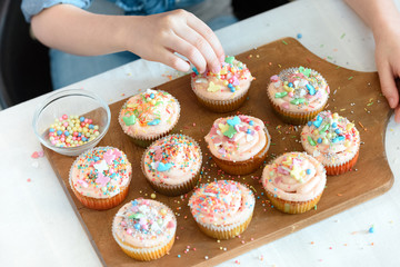 high angle view of girl decorating cupcakes on board with confetti