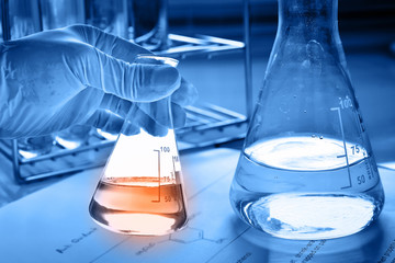 Flask in scientist hand with test tubes in laboratory  