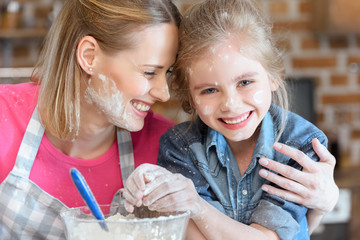portrait of smiling mother and daughter cooking at home
