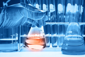 Flask in scientist hand with test tubes in laboratory  