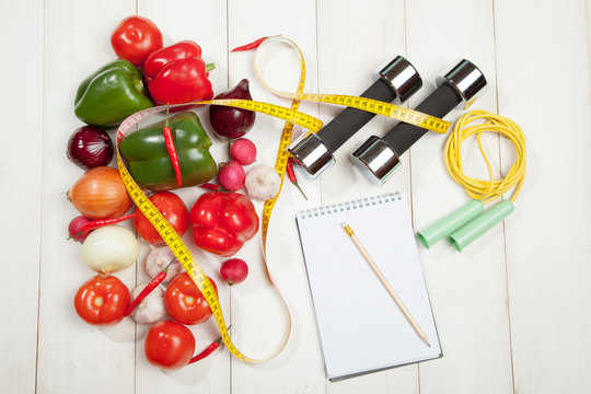 Sport and diet. Healthy lifestyle. Vegetables, dumbbells  notebook. Peppers, tomatoes, garlic, onions  radishes on a white background
