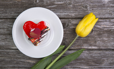 The dish with the cake and flowers on old wooden background