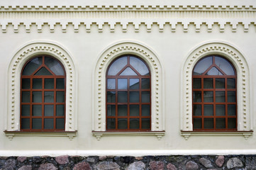 Three brown old arched windows on a white wall plaster.