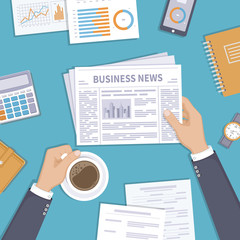 Business news. Businessman holding a newspaper and coffee cup on the desktop. Coffee break, breakfast, lunch, documents, purse, calculator, notebook, wrist watch. View from above
