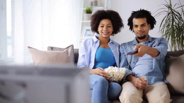 smiling couple with popcorn watching tv at home