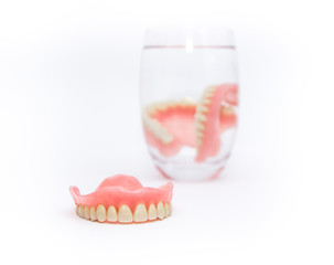 Acrylic dentures immersed in a glass of water,white background.