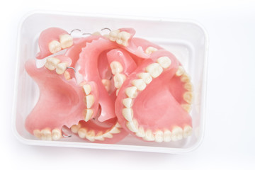 A few acrylic dentures in container, isolated on white background.