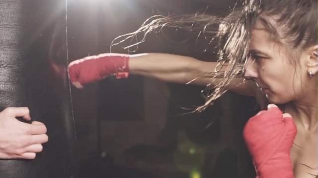 Beautiful Female Punching A Boxing bag With Boxing Gloves at the gym. Concept about sport, fitness, martial arts and people