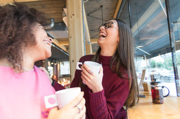 Two young women having fun drinking coffee at the bar
