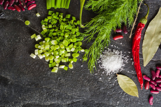 Arrangement of chives, onions, beans and dill on a black background stone slate.