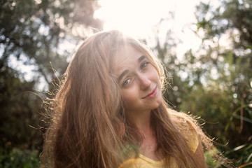 Smiling girl posing in front of high trees in a park retro color backlit shot