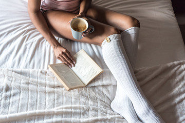 black woman on bed reading a book and drinking coffee with socks