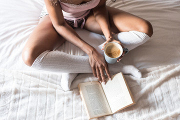 black woman on bed reading a book and drinking coffee with socks