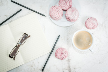 Home spring vacation, relax, work. White stone concrete desk with notepads, pencils, coffee and pink berry cakes (Marshmallow) top view copy space