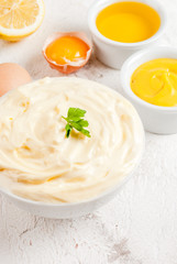 Mayonnaise with ingredients for cooking - eggs, vegetable oil, mustard, lemon, parsley. On the white stone concrete table copy space