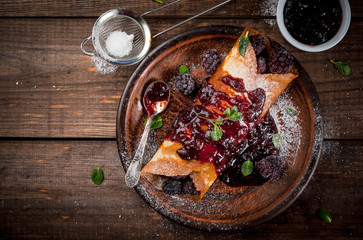 Delicious homemade breakfast: french crepes with forest fruit, topped with jam and filled with forest fruit, sugar and mint, top view, wooden table