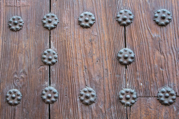 A close-up view to a part of old brown wooden door with metal rivets.