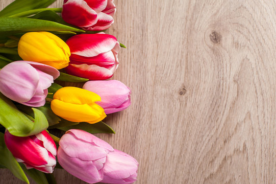 The composition of tulips of different colors on a wooden background, greeting card with free place for inscriptions on any holiday