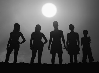 Silhouettes of teenage boys and girls standing on the beach on sunny summer day in black and white