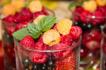 Yellow and red raspberries and a sprig of mint in a glass beaker.