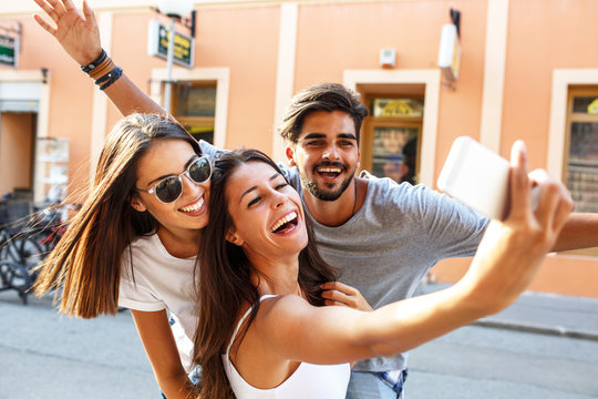 Group of happy young friends having fun on city street.Taking selfie.