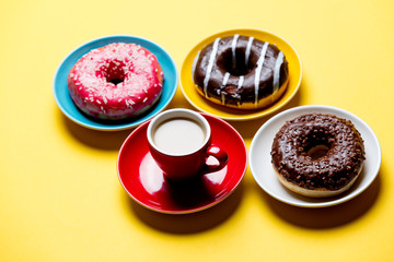 tasty glazed donuts and cup of coffee on plates on the wonderful yellow background