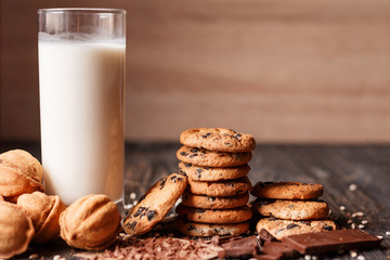 Cookies with chocolate chip and cookies in the shape of nut with glass of milk for breakfast on a dark wooden table