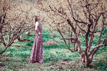 Portrait of a young blond woman in a pink dress on a background of flowering trees