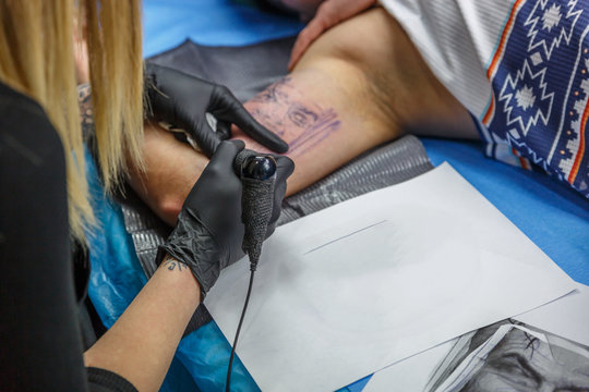 A tattoo artist woman is depicting a tattoo on a boy´s arm