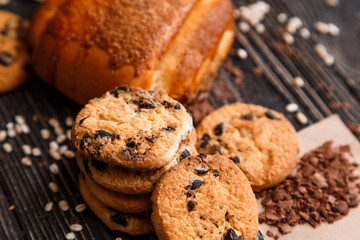 Stacked chocolate chip cookies and cinnamon bun with chocolate on brown napkin.