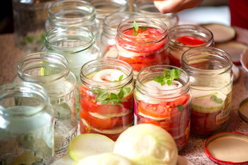 Fototapeta na wymiar Canning fresh tomatoes with onions for winter in jelly marinade. A shot of basil leaves on top of a red ripe tomato slices and onion rings being put in jar.