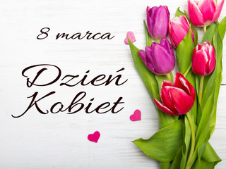 Women's day card with Polish words DZIEŃ KOBIET.Tulip flower and small heart on white wooden background, copy space
