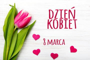 Women's day card with Polish words DZIEŃ KOBIET. Tulip flower small hearts on white wooden background.