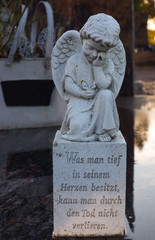trauriges engelchen sitzt auf einem stein mit grabinschrift