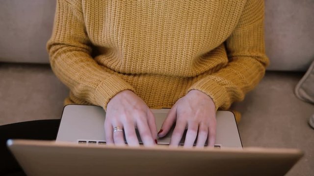 Female hands working on laptop sitting on the couch at home and typing. Fop view of woman holding computer.